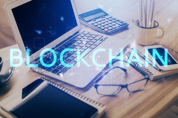 Doble exposición del holograma temático blockchain y criptoeconomía y mesa con fondo de computadora Concepto de criptomoneda bitcoin