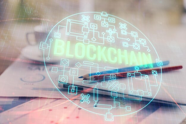 Doble exposición del holograma temático blockchain y criptoeconomía y mesa con fondo de computadora Concepto de criptomoneda bitcoin