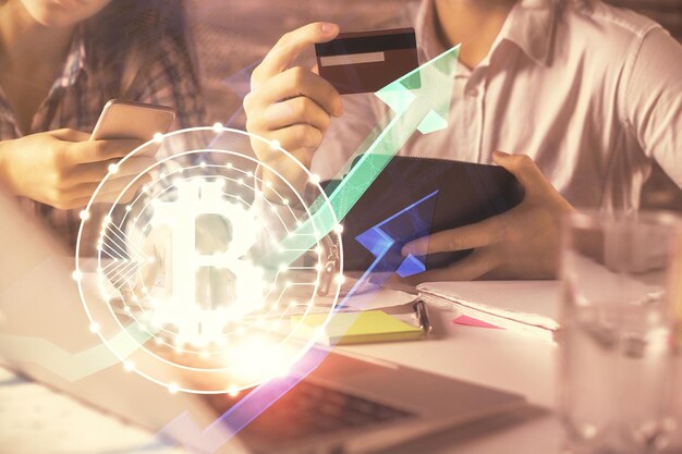 Doble exposición de un hombre y una mujer comprando en línea con una tarjeta de crédito y un holograma de tema criptográfico dibujando el concepto de pago en línea de Blockchain y Ecommerce