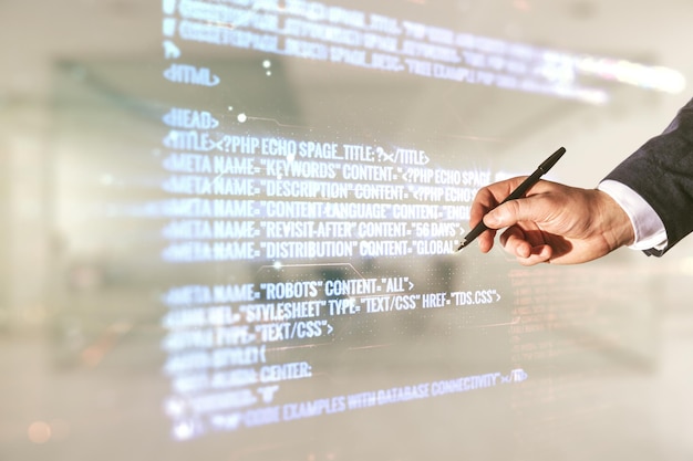 Doble exposición de la mano masculina con bolígrafo que trabaja con una interfaz de lenguaje de programación abstracta en un concepto de investigación y desarrollo de fondo de oficina borroso