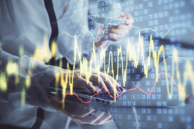 Doble exposición de manos de empresaria escribiendo en computadora y gráfico financiero holograma dibujo concepto de análisis del mercado de valores