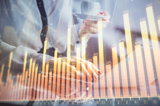 Doble exposición de manos de empresaria escribiendo en computadora y gráfico financiero holograma dibujo concepto de análisis del mercado de valores
