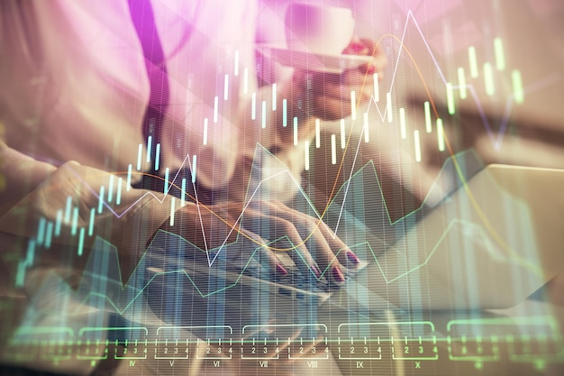Doble exposición de manos de empresaria escribiendo en computadora y gráfico financiero holograma dibujo concepto de análisis del mercado de valores