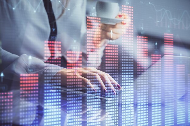 Doble exposición de manos de empresaria escribiendo en computadora y gráfico financiero holograma dibujo concepto de análisis del mercado de valores