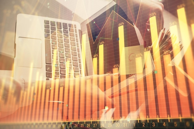 Doble exposición de manos de empresaria escribiendo en computadora y gráfico financiero holograma dibujo concepto de análisis del mercado de valores