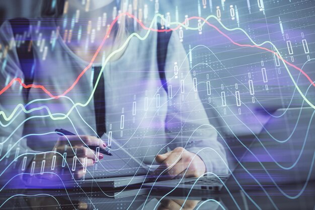 Doble exposición de manos de empresaria escribiendo en computadora y gráfico financiero holograma dibujo concepto de análisis del mercado de valores