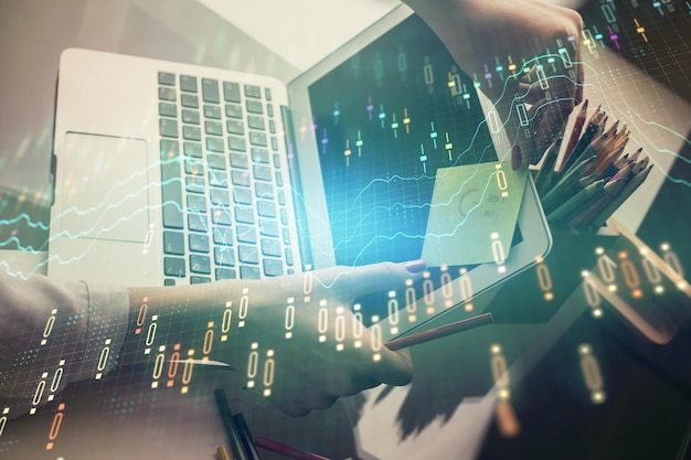 Doble exposición de manos de empresaria escribiendo en computadora y gráfico financiero holograma dibujo concepto de análisis del mercado de valores
