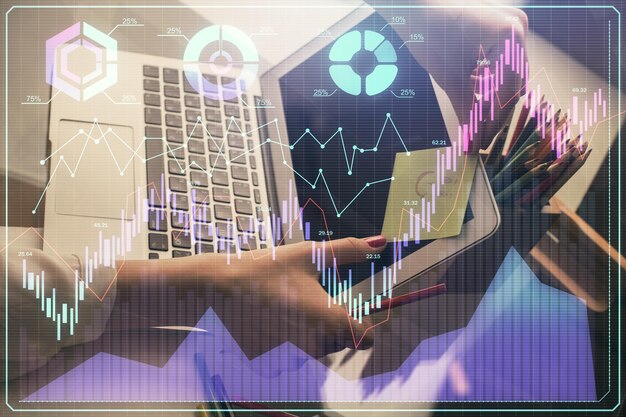 Doble exposición de manos de empresaria escribiendo en computadora y gráfico financiero holograma dibujo concepto de análisis del mercado de valores