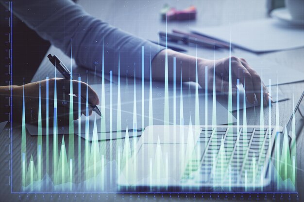 Doble exposición de manos de empresaria escribiendo en computadora y gráfico de forex dibujo de holograma Concepto de análisis financiero