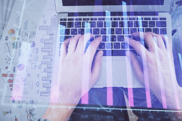 Doble exposición de las manos del hombre escribiendo en el teclado de la computadora portátil y dibujo de hologramas de gráficos de divisas Vista superior Concepto de mercados financieros