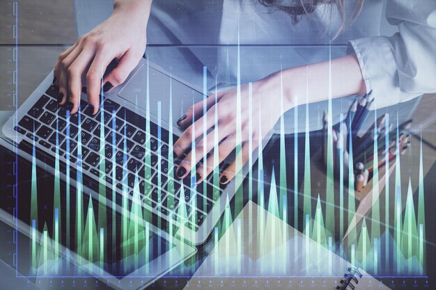 Doble exposición de las manos de la mujer escribiendo en la computadora y dibujo de hologramas de gráficos de divisas Concepto de inversión en el mercado de valores