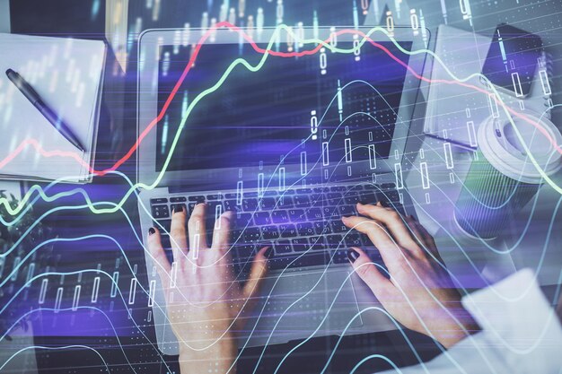 Doble exposición de las manos de la mujer escribiendo en la computadora y dibujo de hologramas de gráficos de divisas Concepto de inversión en el mercado de valores