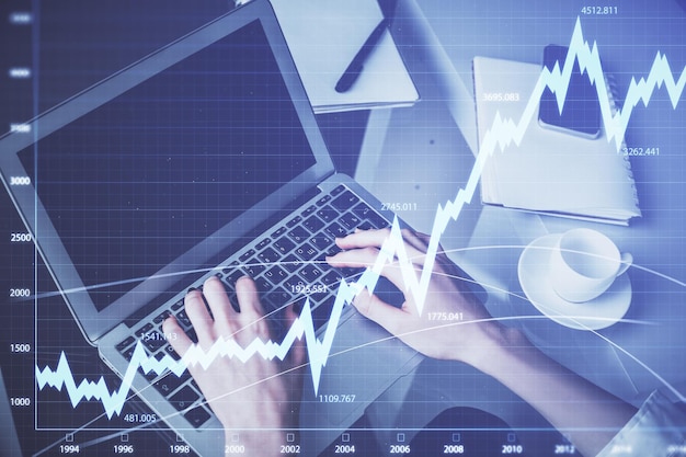 Doble exposición de las manos de la mujer escribiendo en la computadora y dibujo de hologramas de gráficos de divisas Concepto de inversión en el mercado de valores