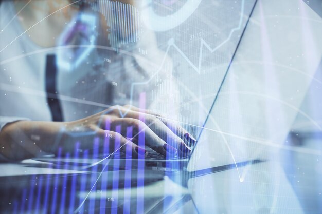 Doble exposición de manos de mujer escribiendo en computadora y gráfico financiero holograma dibujo concepto de análisis del mercado de valores