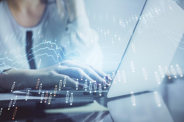 Doble exposición de manos de mujer escribiendo en computadora y gráfico financiero holograma dibujo concepto de análisis del mercado de valores