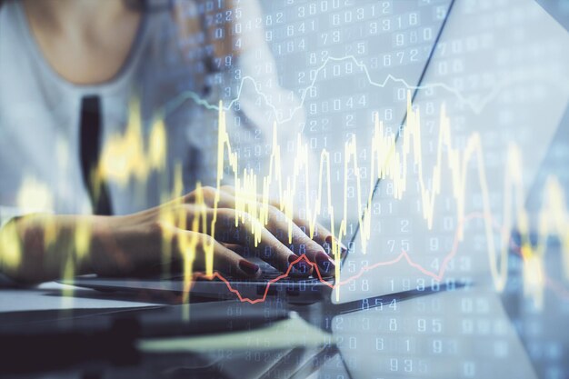 Doble exposición de manos de mujer escribiendo en computadora y gráfico financiero holograma dibujo concepto de análisis del mercado de valores