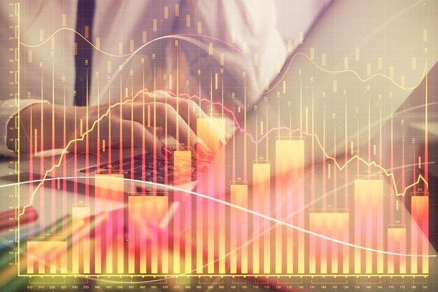 Doble exposición de manos de mujer escribiendo en computadora y gráfico financiero holograma dibujo concepto de análisis del mercado de valores