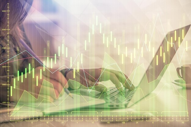Doble exposición de las manos de una mujer de negocios escribiendo en la computadora y dibujando un holograma de gráficos de divisas Concepto de análisis financiero