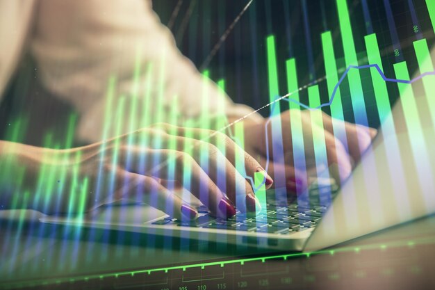 Doble exposición de las manos de una mujer de negocios escribiendo en la computadora y dibujando un holograma de gráficos de divisas Concepto de análisis financiero