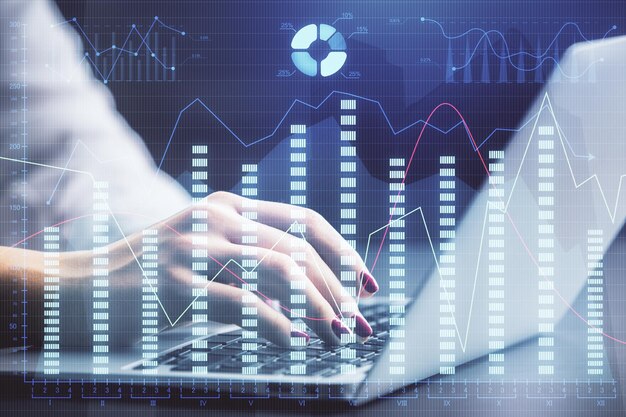 Doble exposición de las manos de una mujer de negocios escribiendo en la computadora y dibujando un holograma de gráficos de divisas Concepto de análisis financiero