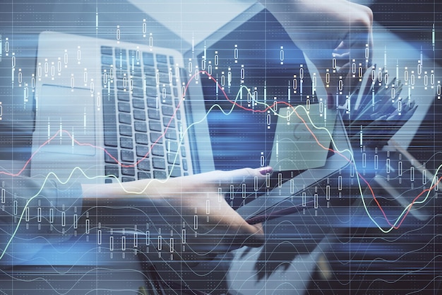 Doble exposición de las manos de una mujer de negocios escribiendo en la computadora y dibujando un holograma de gráficos financieros Concepto de análisis del mercado de valores