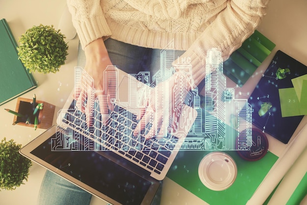 Foto doble exposición de manos de mujeres trabajando en computadoras y dibujos de hologramas de construcción de edificios top view concepto de ciudad inteligente