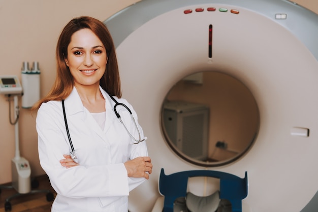 Foto doc feminino no jaleco perto da máquina de tomografia.