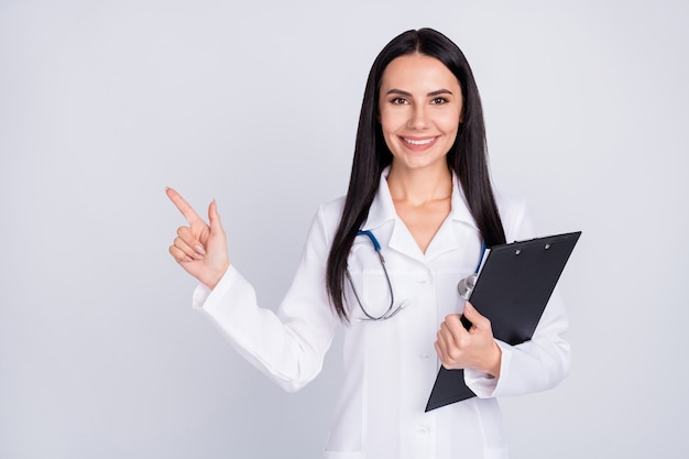 Doc senhora de jaleco branco segurando a prancheta apontar dedo espaço vazio fundo cinza