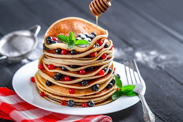 Doce assado panquecas caseiras com frutas, hortelã e açúcar em pó, derramando com mel no delicioso café da manhã.