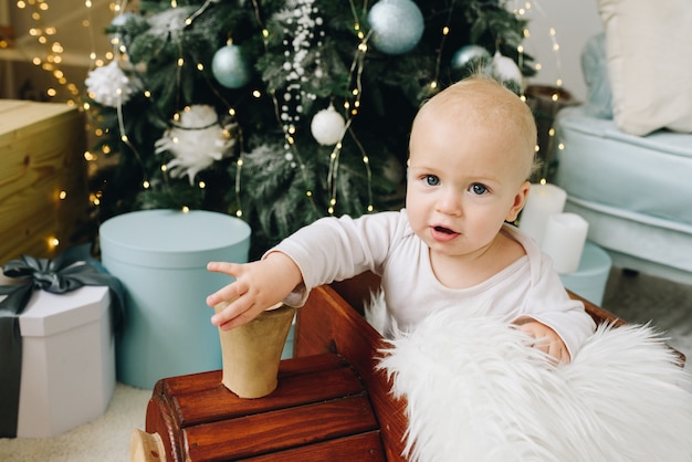 Doce bebê caucasiano sentado em um trem de brinquedo de madeira perto da árvore de Natal decorada