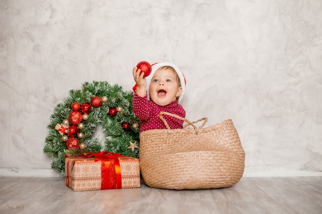Doce bebê Papai Noel sentado em uma cesta de vime com uma caixa de presente