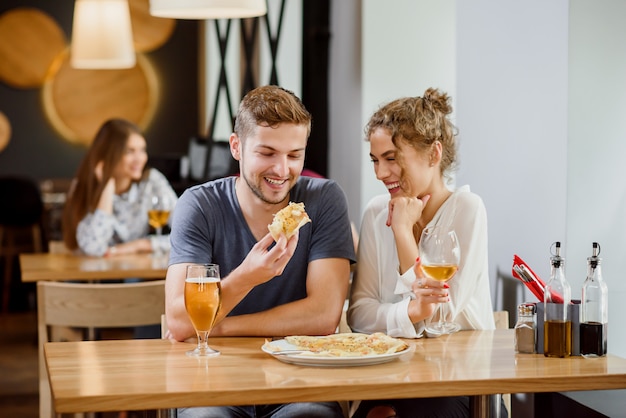 Doce casal comendo pizza e bebendo cerveja e vinho na pizzaria.