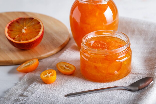 Doce da laranja e do kumquat em um frasco de vidro com frutos frescos em uma toalha de mesa de linho branca.