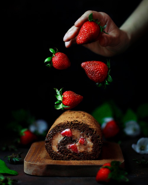 Doce de morango chocolate roll com levitando morangos e mãos de mulher, fotografia de comida escura