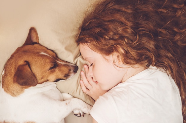 Doce encaracolado menina e cachorro está dormindo na noite.