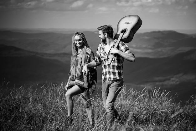 Doce harmonia nas montanhas. Casal de viajantes felizes passeando, sorrindo e tocando violão