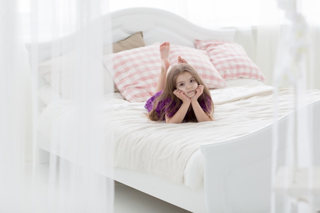 Doce jovem de vestido roxo na cama com coxins