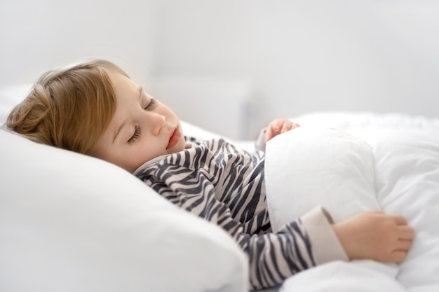 Doce loira caucasiana adorável bebê menina dormindo na cama em lençóis brancos sob quente bl