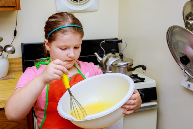 Doce menina bonita está aprendendo a fazer um bolo, na cozinha de casa