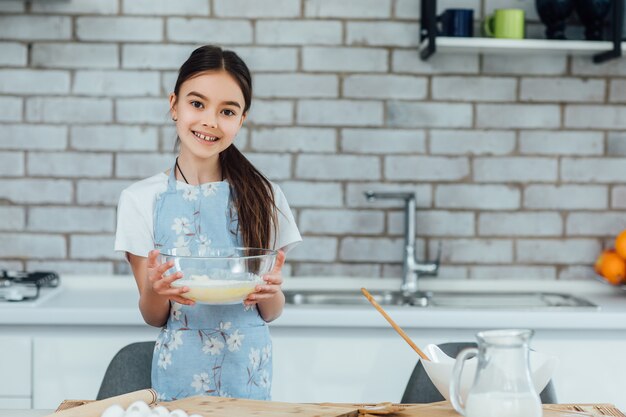 Doce menina bonitinha está aprendendo a fazer um bolo, na cozinha de casa, conceito de família