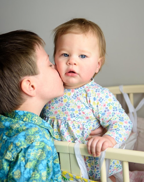 Doce menina de dez meses sentada em um berço brincando com seu irmão Um irmão e uma irmã amorosos Feliz infância