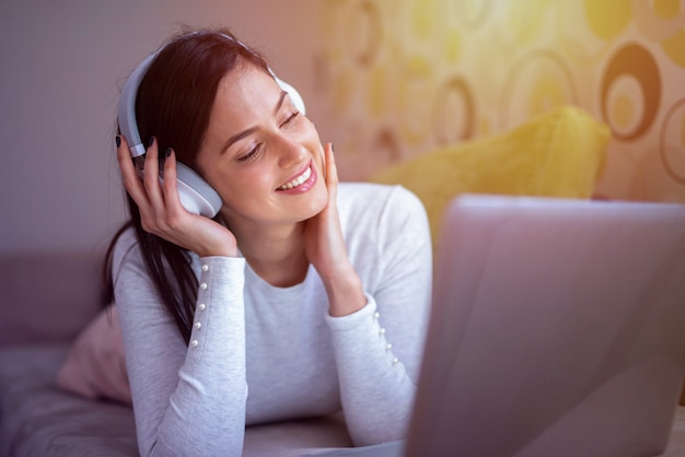 Doce menina deitada em sua cama com fones de ouvido na cabeça dela. Ouvindo música e descansando.