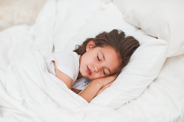 Doce menina, dormindo tranquilamente na cama com as mãos debaixo da cabeça