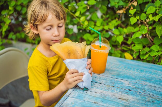 Doce menino caucasiano comendo panquecas e bebendo suco de laranja