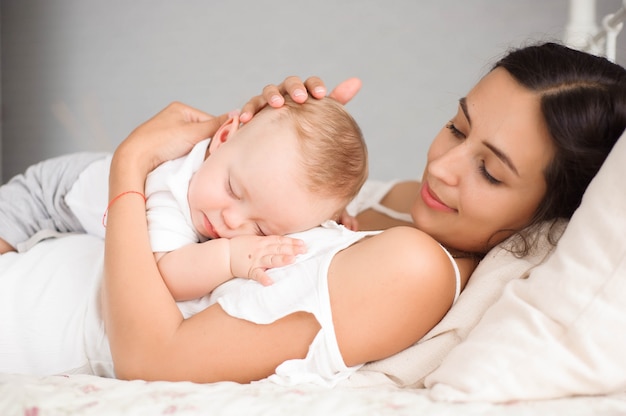 Doce menino dormindo na cama com sua mãe