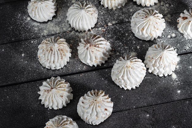 Doce merengue sobremesa deliciosa e leve Fundo culinário com merengue de baunilha no fundo escuro de madeira polvilhado com nozes cacau e açúcar em pó Ainda vida em estilo de comida