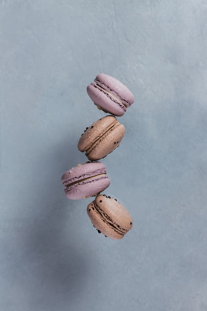 Doces biscoitos franceses caindo em movimento na superfície cinza. Cookies de macaroons voadores coloridos pastel. Conceito de comida, culinária e culinária