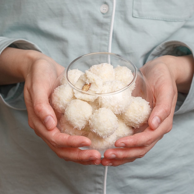 Foto doces caseiros vegan. bolas de coco branco em uma tigela de vidro nas mãos de uma mulher, close-up