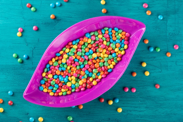 Doces de confetes coloridos em uma tigela com superfície azul.