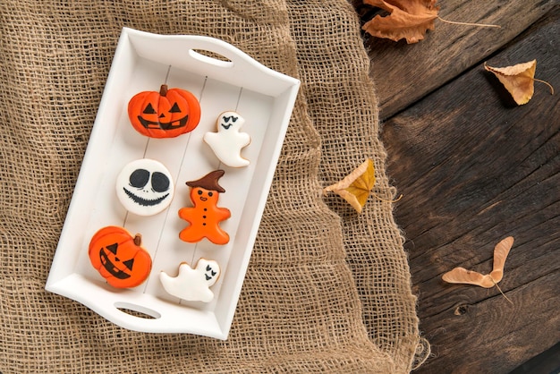 Doces de Halloween estão em uma bandeja de madeira Pão de gengibre laranja em forma de abóbora e fantasmas Biscoito saboroso na mesa Vista superior